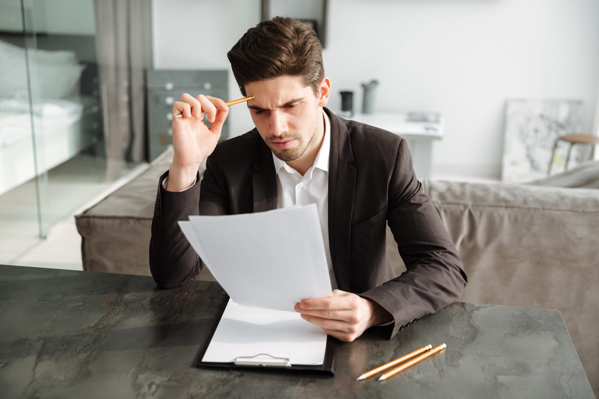 A man at a desk reading through a printed document, a pencil in his hand